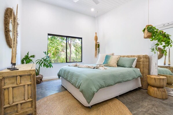 A bedroom with a bed, a large window, and a hanging plant.