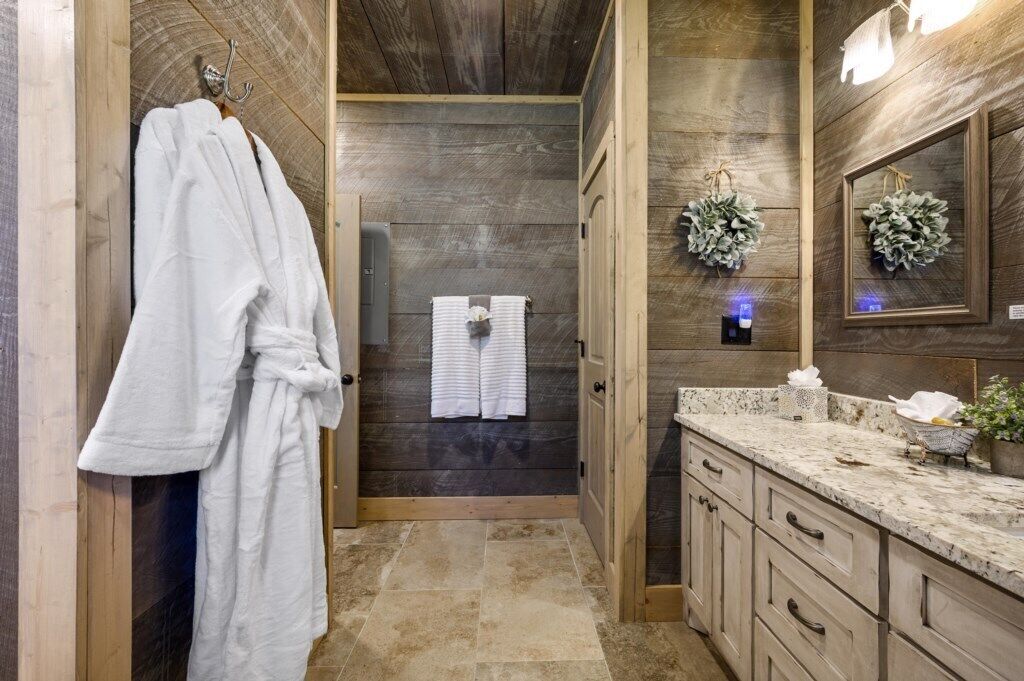 A bathroom with wooden walls, a marble countertop, and a white robe hanging on a rack.