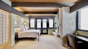 Une chambre à coucher avec un lit, un bureau et une chaise. Il y a des fenêtres et une vue sur l’extérieur.