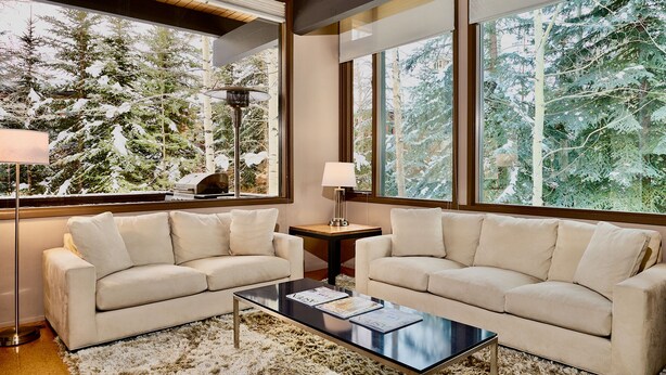 Un salon chaleureux avec deux canapés beige, une table basse et un lampadaire. De grandes fenêtres offrent une vue sur des arbres couverts de neige.