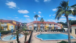 Un complejo turístico con varias edificaciones, una piscina central y palmeras.