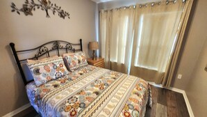 Un dormitorio con cama, cortinas, una mesita de noche y un adorno en la pared.
