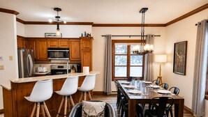 Una cocina moderna con armarios de madera, un refrigerador de acero inoxidable y un comedor con una mesa larga y sillas.