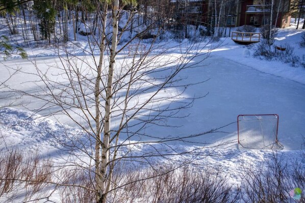 A snow-covered outdoor area with a hockey goal and a wooden structure in the background.