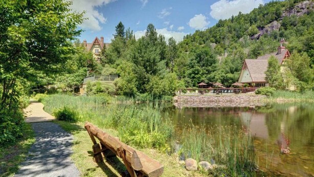 Un sendero junto al lago con un banco de madera, un pequeño muelle y un edificio con techo rojo.