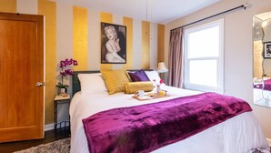 A hotel room with a bed, a bedside table with a lamp, a window with curtains, and a mirror on the wall.