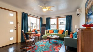 A living room with a wooden floor, a green sofa, a rocking chair, and a colorful rug.
