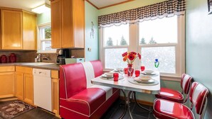 A compact kitchen with wooden cabinets, a red diner-style booth, and a dining table set for four.