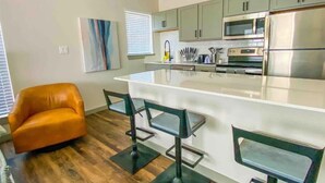 A modern kitchen with a central island, bar stools, and a leather chair. - Cozy Studio Walk to Lower Greenville Dallas - Pet-Friendly, W/D, BBQ, Parking (Dallas)