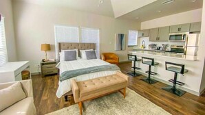 A modern bedroom with a large bed, a bench, a desk, and a kitchenette. - Cozy Studio Walk to Lower Greenville Dallas - Pet-Friendly, W/D, BBQ, Parking (Dallas)