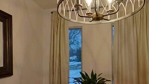A dining area with a wooden table, a potted plant, and a modern chandelier.