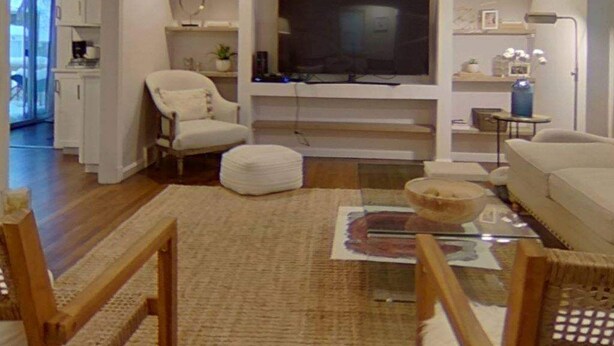 A modern living room with a flat-screen TV, white sofas, a glass coffee table, and wooden beams on the ceiling.