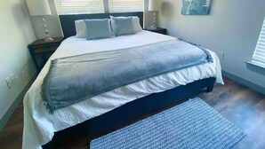Ein Schlafzimmer mit einem großen Bett, zwei Nachttischlampen, einem Teppich und einem Fenster mit Jalousien.