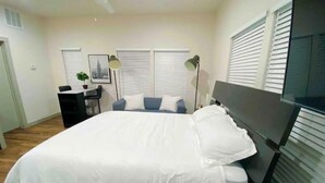 Une chambre avec un grand lit, un bureau, deux chaises, une lampe sur pied et un téléviseur.