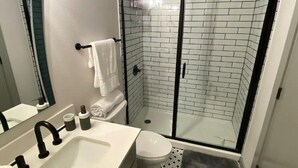 Une salle de bain moderne avec un lavabo blanc, des robinets noirs, des toilettes et une douche en verre, le tout agrémenté d’un mur carrelé.