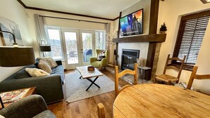 A living room with a sofa, a wooden coffee table, a TV mounted on the wall, and a fireplace. - Superb ski in/out - Ask about summer pool access! (Mont-Tremblant)