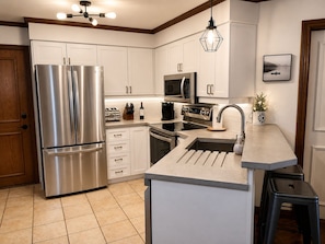 A modern kitchen with stainless steel appliances, white cabinetry, a central island with a sink, and a hanging light fixture.