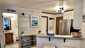 A modern kitchen with a wooden accent wall, a BANI National Park poster, a bar stool, and a refrigerator. - Superb ski in/out - Ask about summer pool access! (Mont-Tremblant)