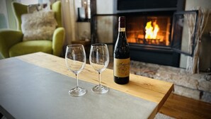 A wooden table with two empty wine glasses and a bottle of wine in a cozy room with a fireplace. - Superb ski in/out - Ask about summer pool access! (Mont-Tremblant)