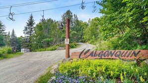 A wooden sign with the name 'Calgonquinn' surrounded by greenery and a dirt road. - Superb ski in/out - Ask about summer pool access! (Mont-Tremblant)