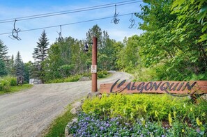 A wooden sign with the name 'Calgonquinn' surrounded by greenery and a dirt road. - Superb ski in/out - Ask about summer pool access! (Mont-Tremblant)