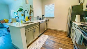 Una cocina moderna con una isla central, piso de madera y una pequeña zona de comedor con un sofá azul.
