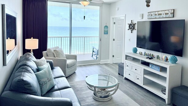 Sala de estar con sofá, televisión y una mesa de centro de vidrio. Balcón con vista al océano.