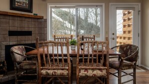 A dining area with a wooden table and chairs, a fireplace, and a large window with a view of trees. - Outpost: Pitchfork 432 - Close to Snow King Mtn! (Jackson)