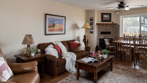 A living room with a brown sofa, a wooden coffee table, a fireplace, and a dining area with wooden chairs and a table. - Outpost: Pitchfork 432 - Close to Snow King Mtn! (Jackson)