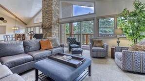 A spacious living room with a stone fireplace, leather sofas, and a large window offering a view of the outdoors. - Beautiful Townhouse near ski slopes, biking trail, & 1 mile from the main street (Park City)