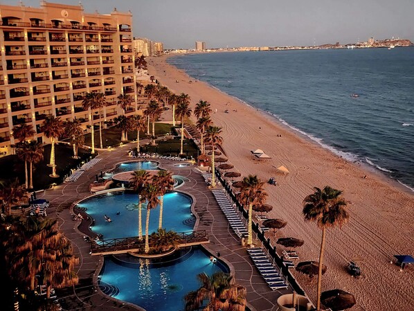 A resort with multiple swimming pools, a beach, and a high-rise hotel.