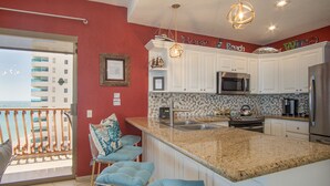 A kitchen with white cabinets, a granite countertop, a stainless steel refrigerator, and a microwave.