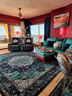A living room with a large patterned rug, a green sofa, a dark armchair, and a red lamp.