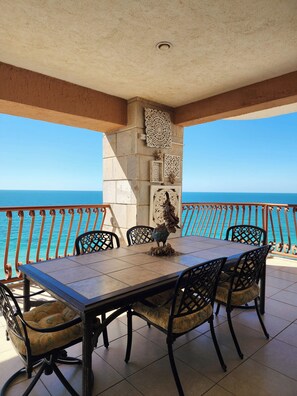 A dining area with a table and chairs, a decorative wall, and a view of the sea.