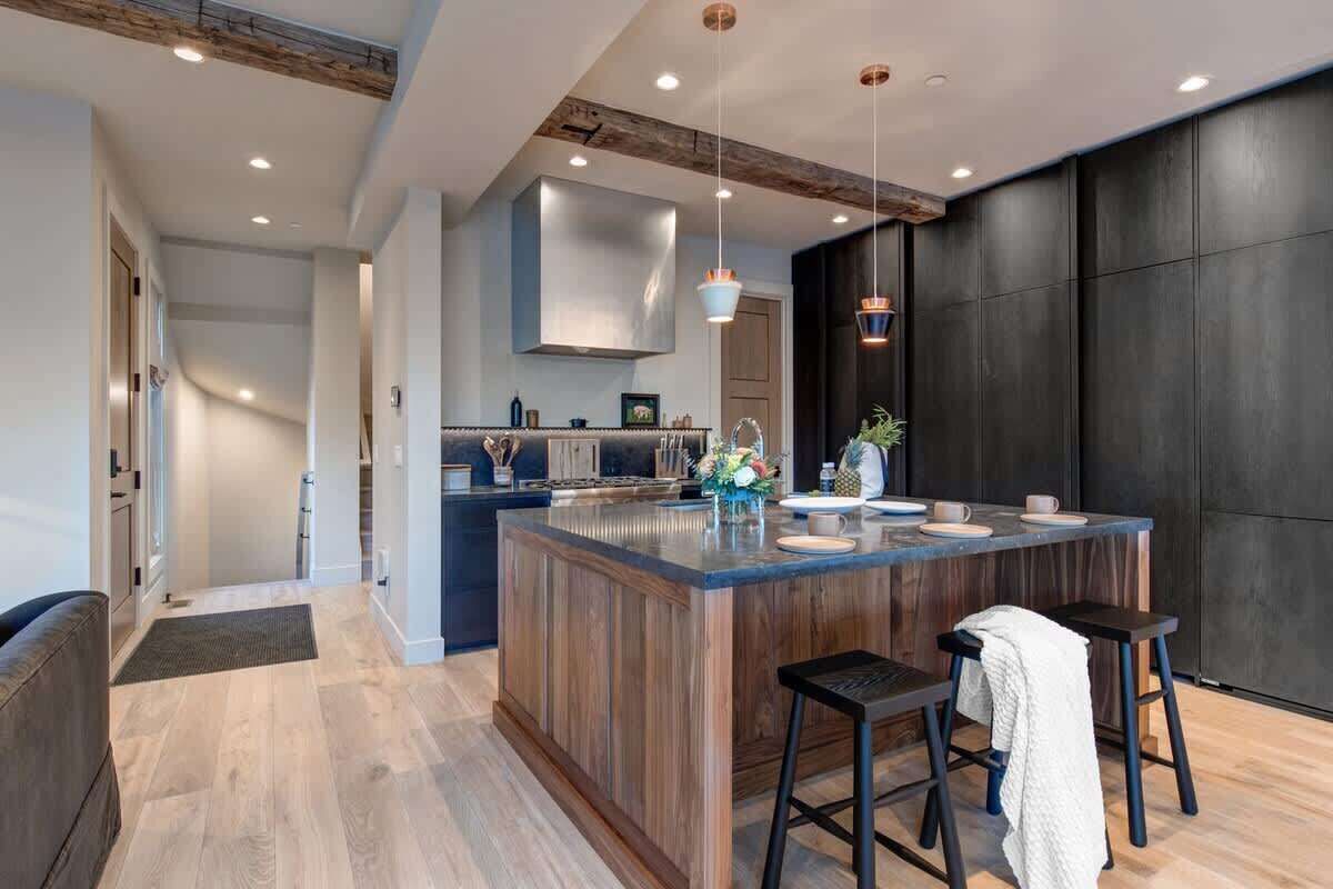 A modern kitchen with a central island, bar stools, pendant lighting, and a dark accent wall.