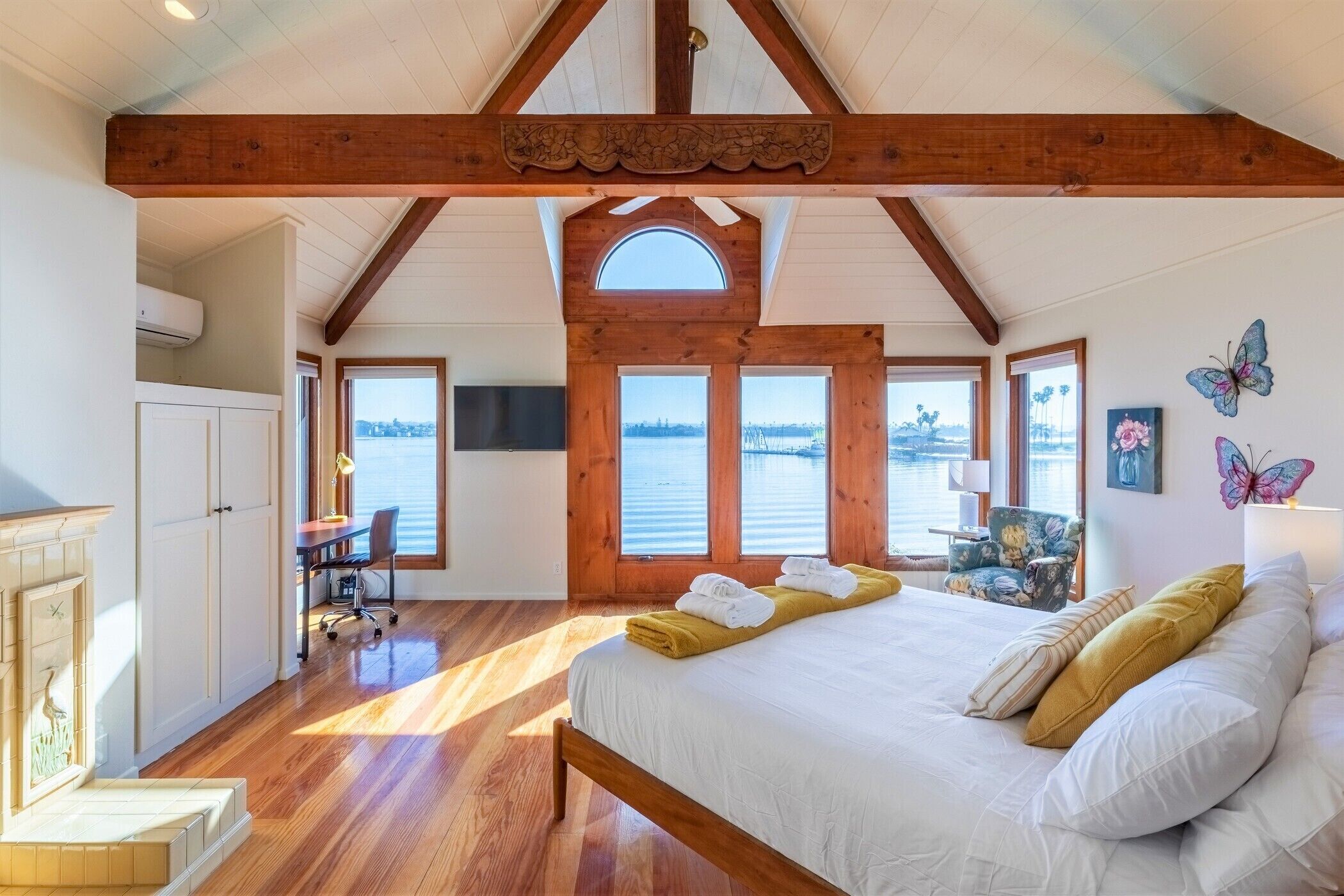 Een slaapkamer met een houten plafond, een groot bed, een bureau en uitzicht op het water.