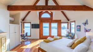 A bedroom with a wooden ceiling, a large bed, a desk, and a view of the water. - Bayside Breeze | Waterfront Patio & Sunset Views (San Diego)