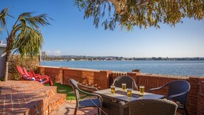 An outdoor patio with wicker furniture, a brick wall, and a view of the sea. - Bayside Breeze | Waterfront Patio & Sunset Views (San Diego)