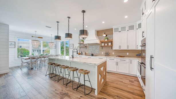 A modern kitchen with white cabinetry, wooden flooring, and a central island with bar stools.