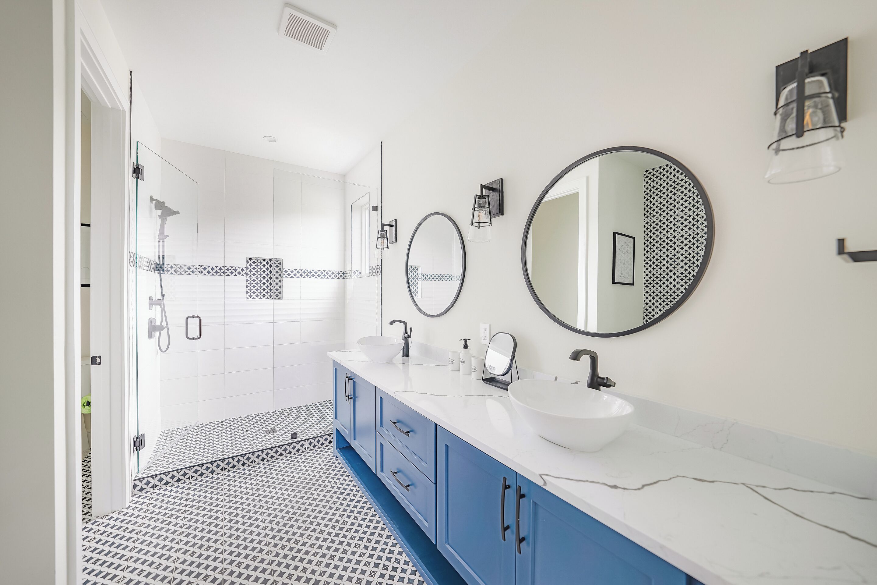Een moderne badkamer met een kleurenschema in wit en blauw, met een groot wastafel, twee spiegels en een douchehoek.