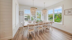 A dining area with a wooden table, white chairs, and two hanging chandeliers.