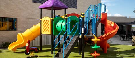 Un parque infantil con tobogán, estructura de escalada y zona cubierta.