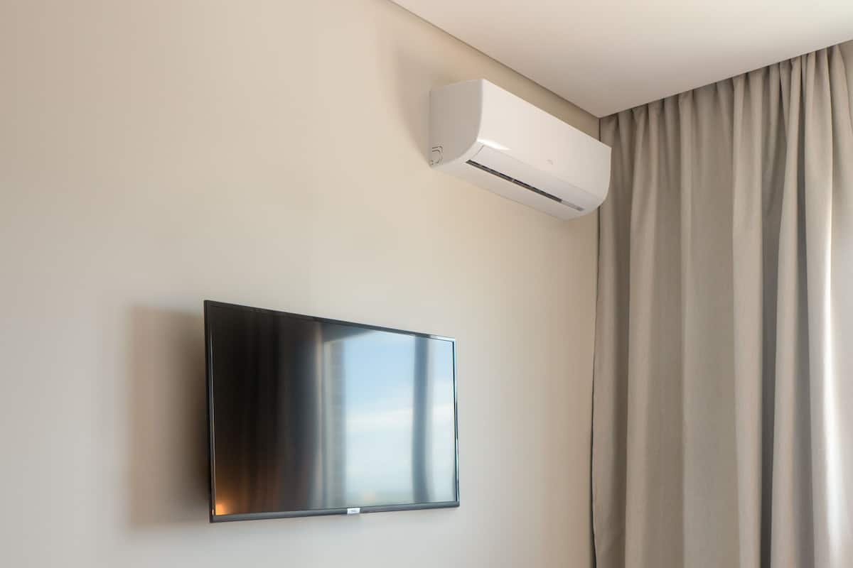Habitación de hotel con cama, televisor de pantalla plana montado y equipo de aire acondicionado en la pared.