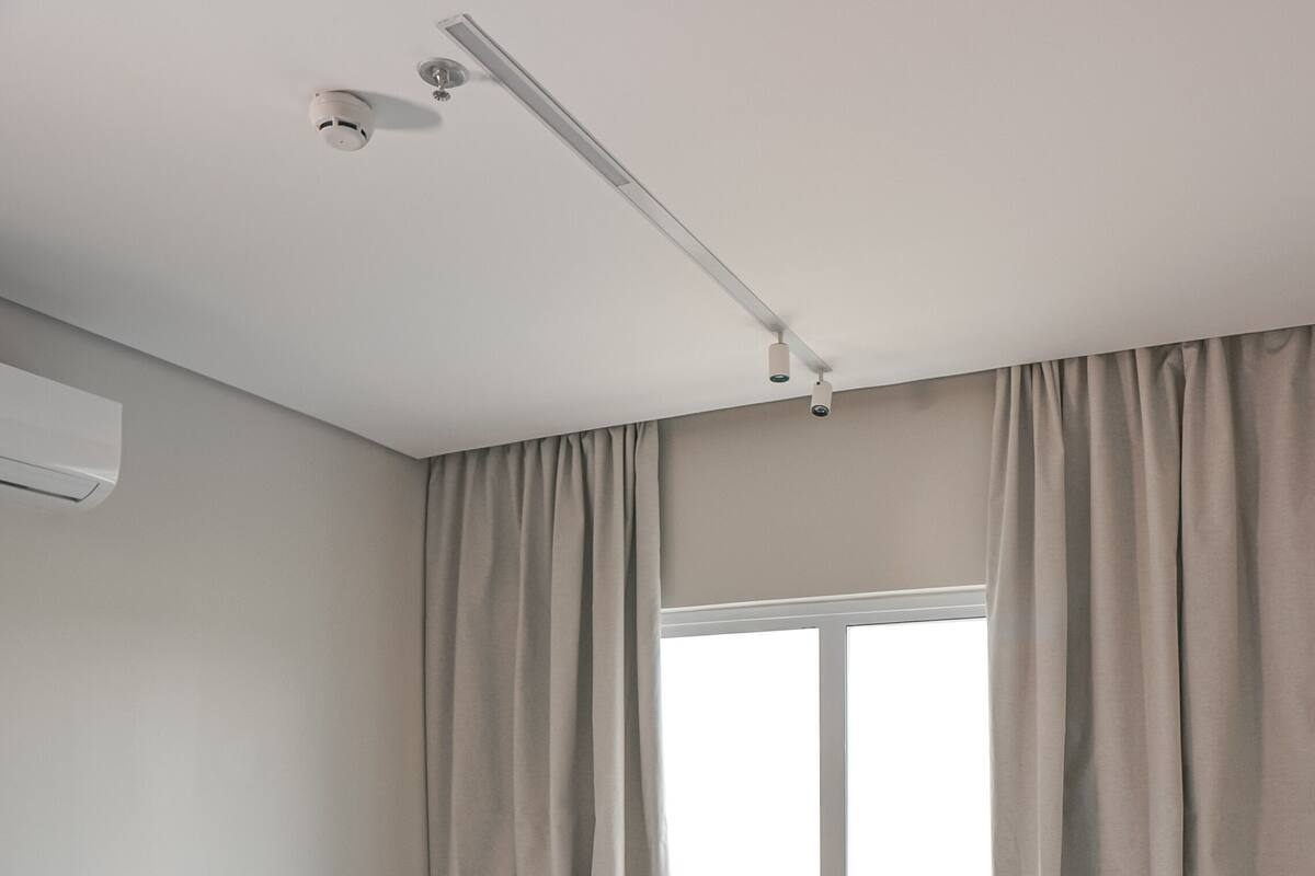 Una habitación pequeña y limpia con dos camas individuales, una ventana con cortinas, una lámpara en el techo y un aire acondicionado instalado en la pared.