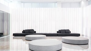 A modern interior with a seating area featuring a sofa and ottomans, a glass partition, and a marble floor. - Exclusive - GAV Hotéis e Resorts (Salinópolis)
