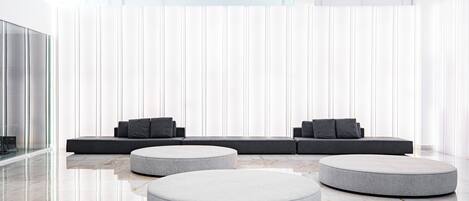 A modern interior with a seating area featuring a sofa and ottomans, a glass partition, and a marble floor.