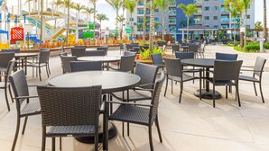 An outdoor seating area with tables and chairs, palm trees, and a large hotel building in the background. - Exclusive - GAV Hotéis e Resorts (Salinópolis)