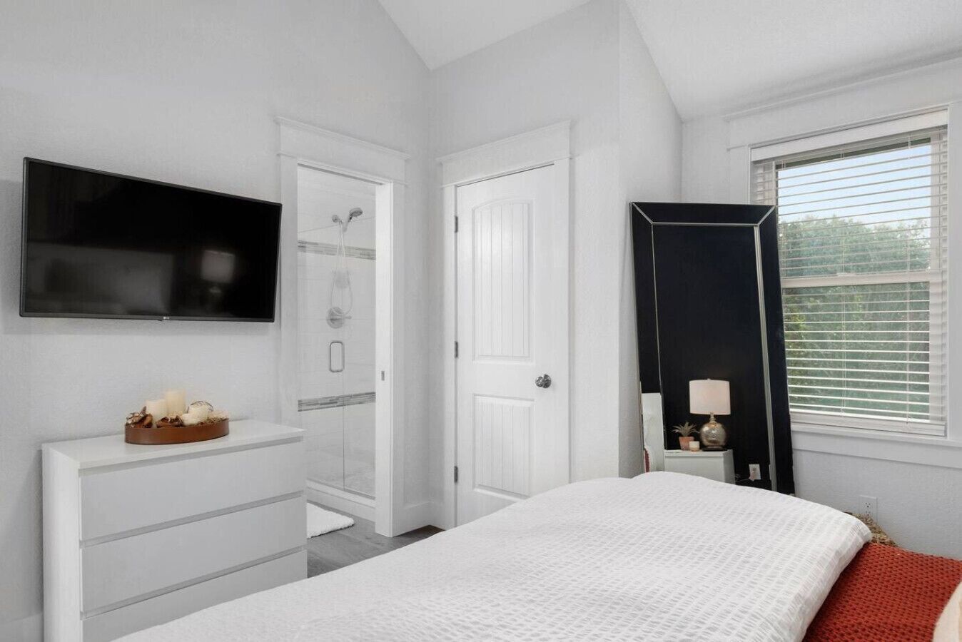 A bedroom with a bed, a dresser, a TV, a door, and a window.