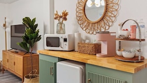 Une cuisine équipée d’un four à micro-ondes, d’un grille-pain et d’une machine à café sur le plan de travail, d’un téléviseur posé sur un meuble et d’un miroir décoratif accroché au mur.