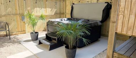 A hot tub with steps, surrounded by potted plants, in a wooden-fenced backyard.